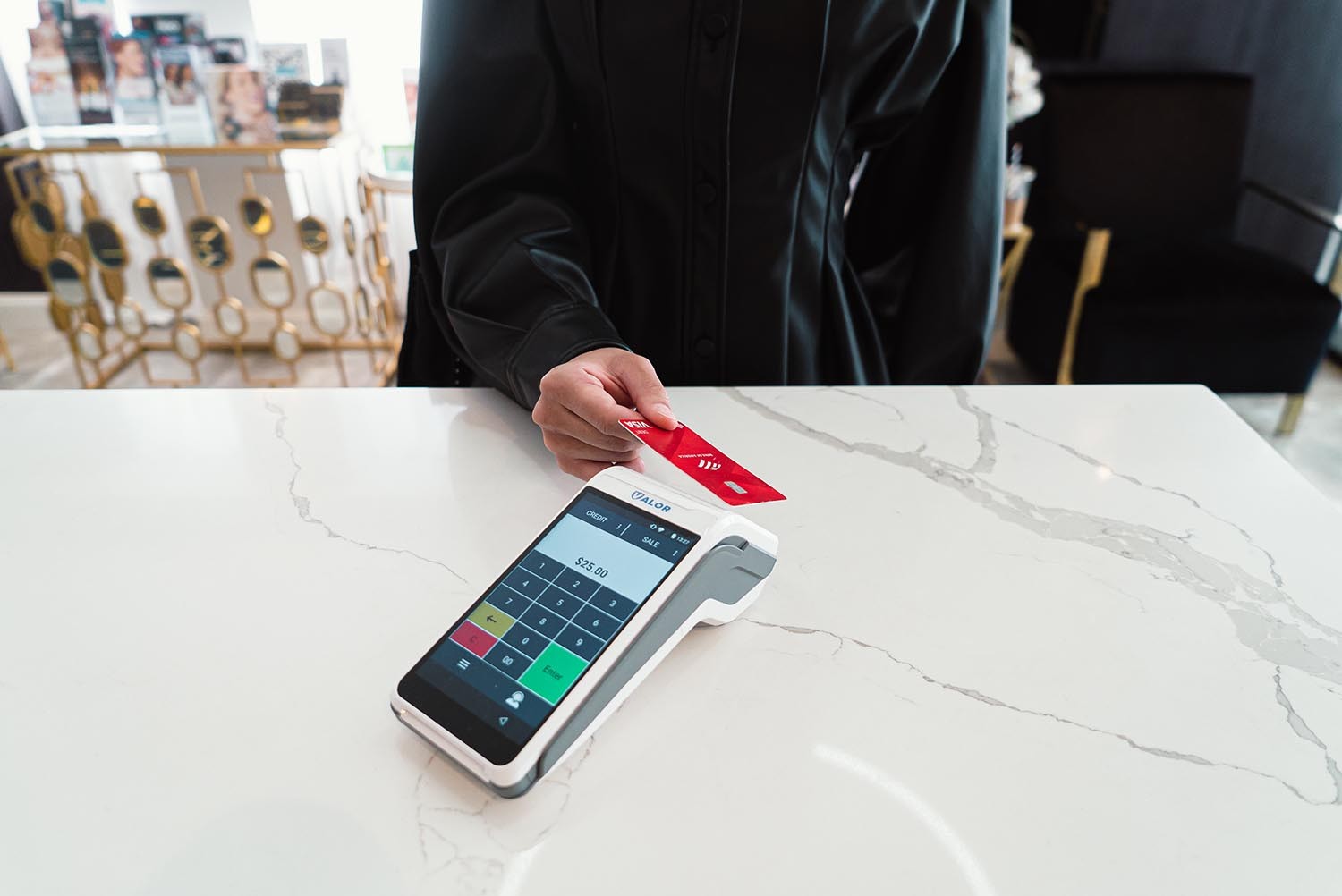 Customer tapping a red card on a Valor terminal at a salon counter